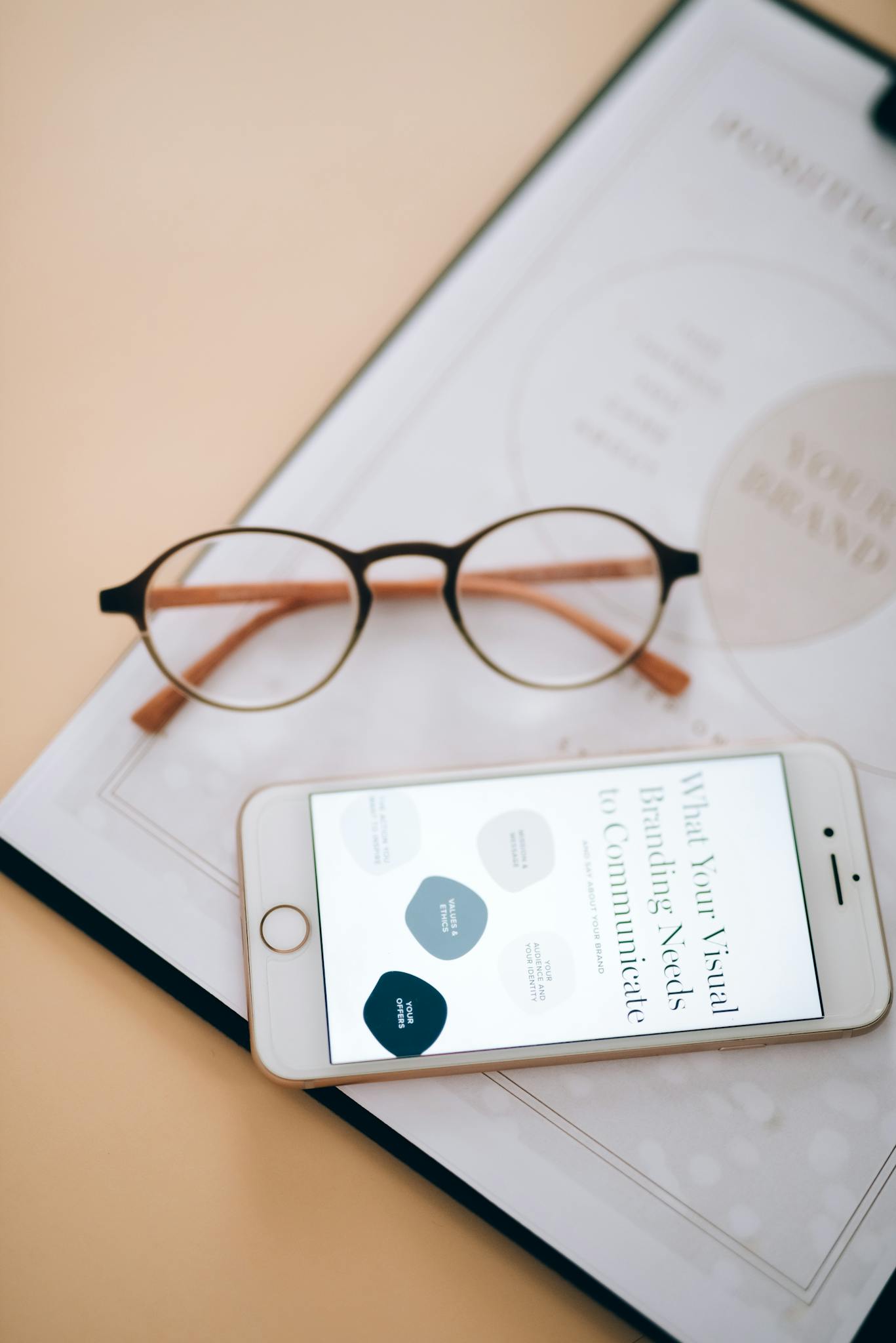 A minimalist flatlay of eyeglasses, smartphone, and a notepad on a desk.