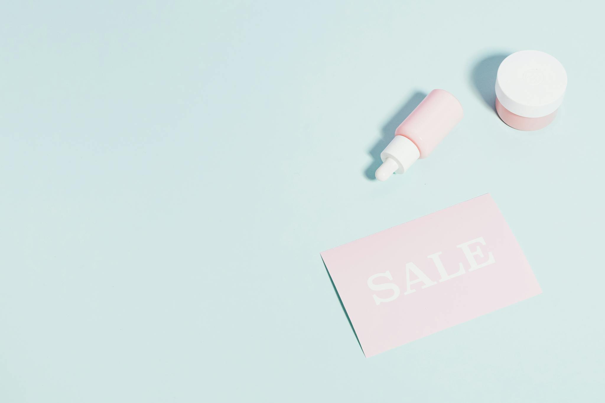 Pink beauty products and sale sign on pastel backdrop.